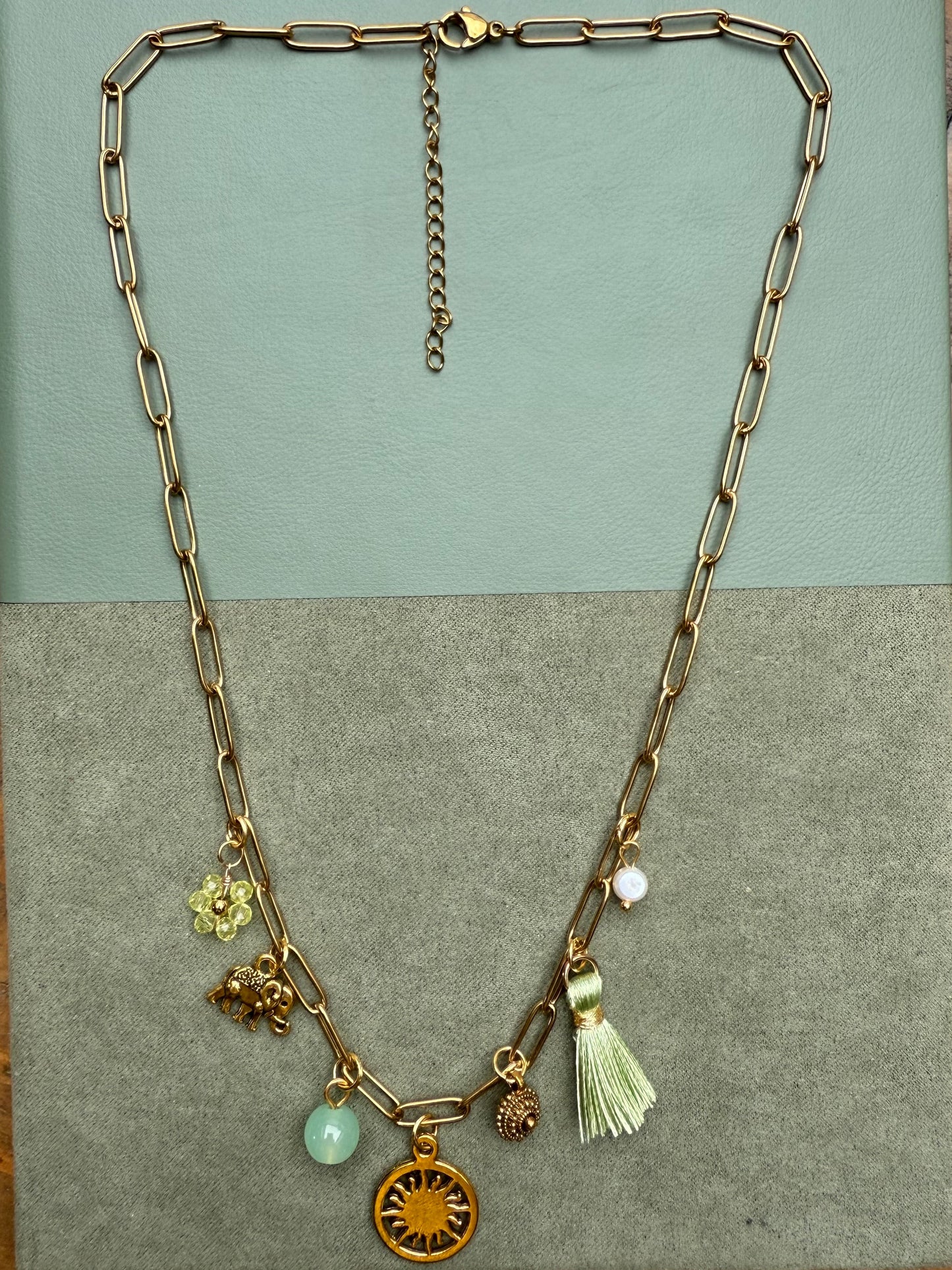 Gold necklace with charms on a two-tone card against a green surface
