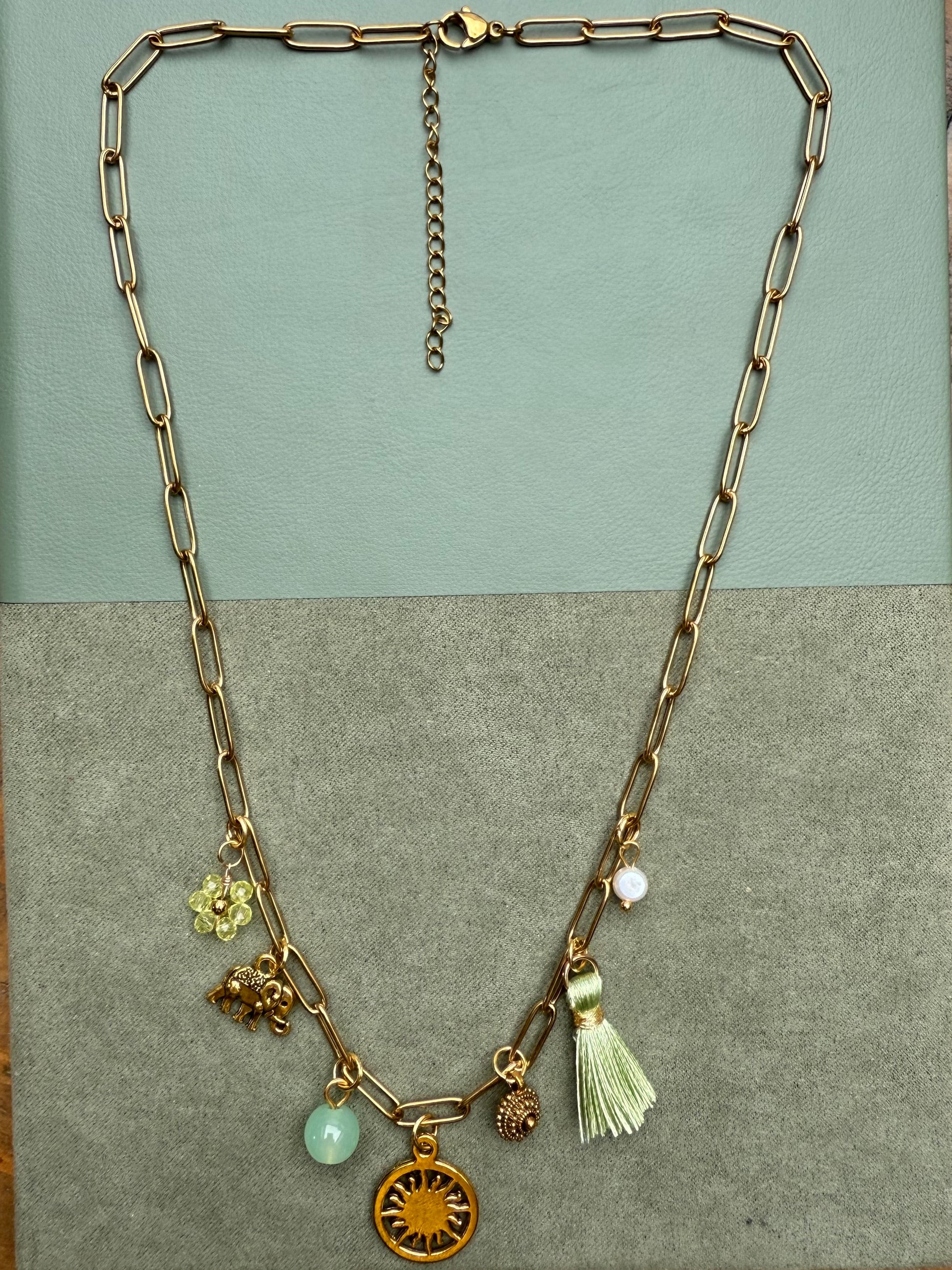 Gold necklace with charms on a two-tone card against a green surface