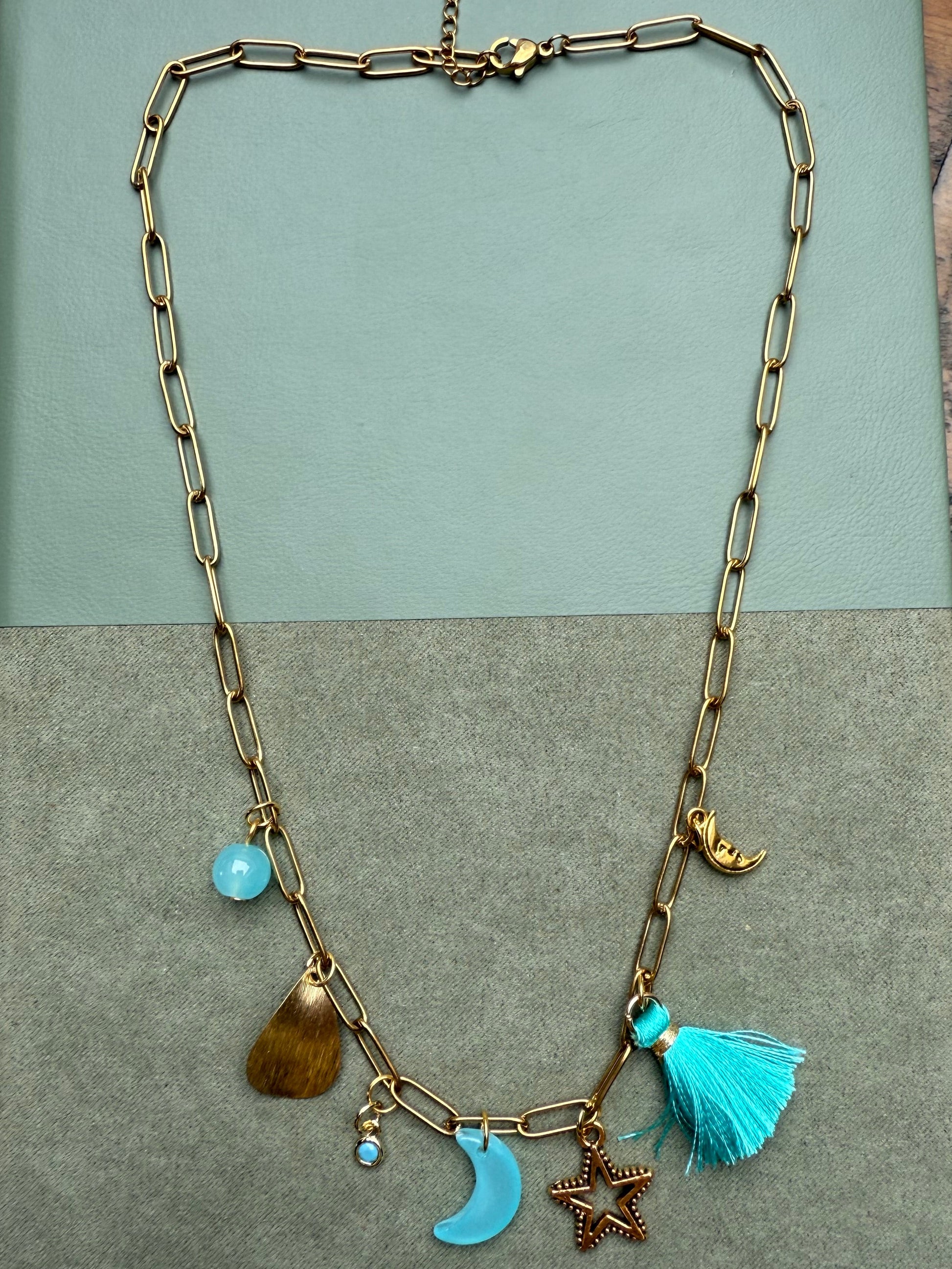 Gold chain necklace with charms on a textured green surface