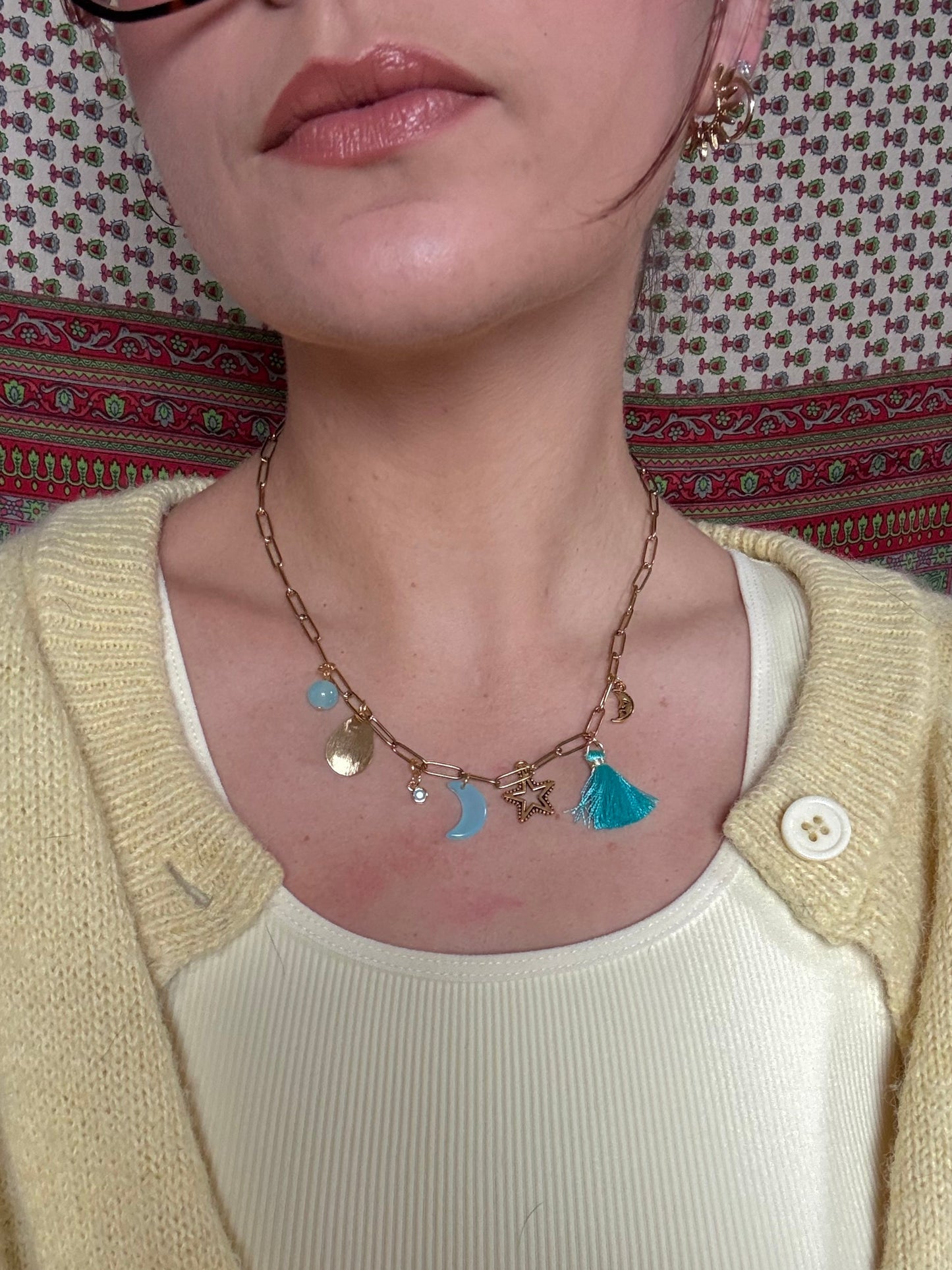 Close-up of a person wearing a yellow sweater and white top with a decorative necklace on a patterned fabric background.