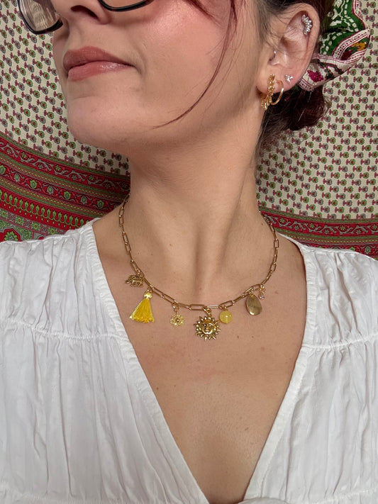 Person wearing a gold necklace with charms on a patterned surface