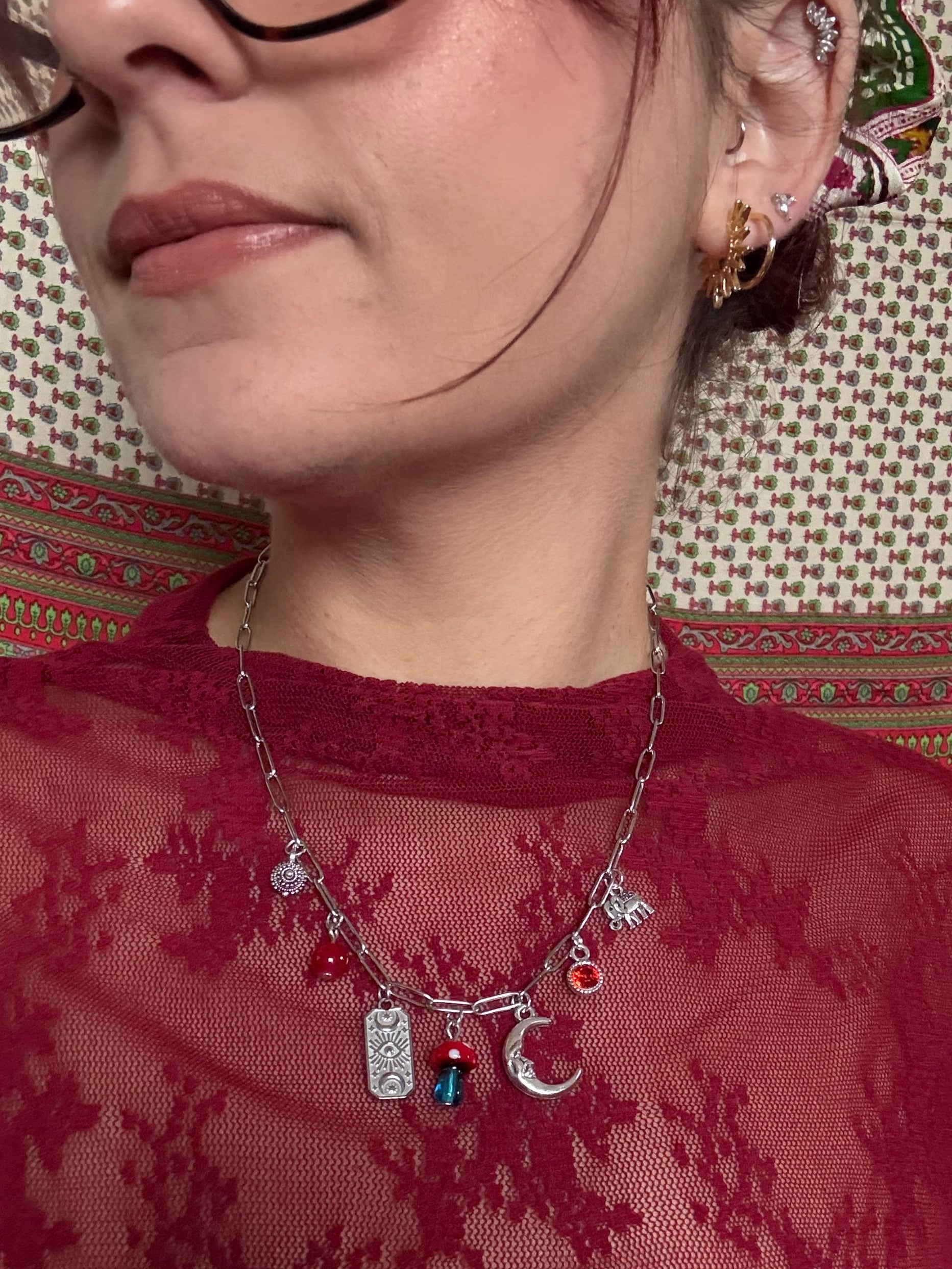 Close-up of a person wearing a red lace garment with a necklace featuring various charms.