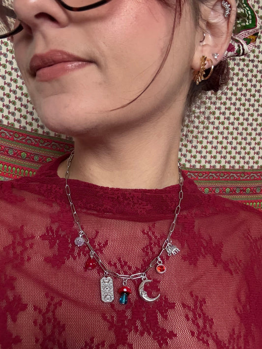 Close-up of a person wearing a red lace garment with a necklace featuring various charms.