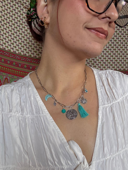 Woman wearing a white blouse and multiple necklaces with charms on a patterned rug.