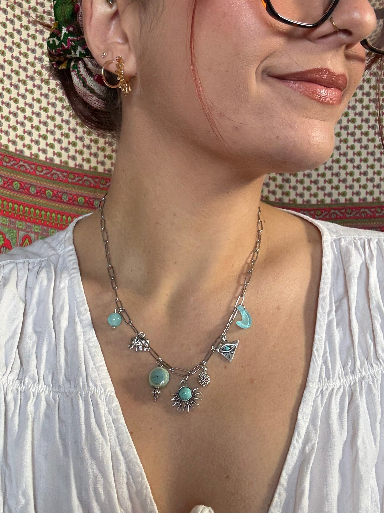 Woman wearing a white top and a decorative necklace with turquoise stones on a patterned rug.